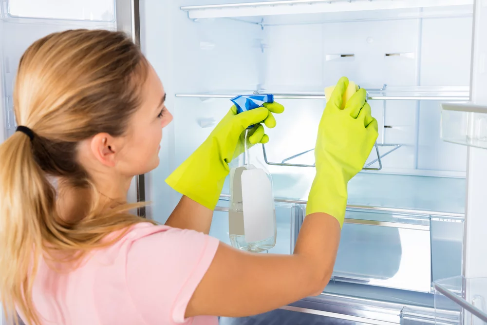 a woman cleans the shelves in the fridge